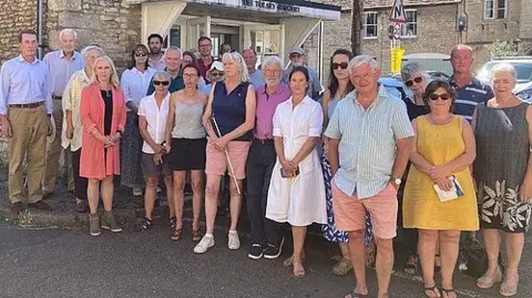 A large group of adults stand outside a surgery building.