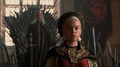 Character in House of Dragons wearing ornate head-dress, necklace and earrings