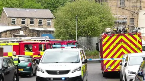 BBC Police vehicles and fire engines at the scene with traditional brick buildings in the background
