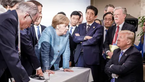 Getty Images Angela Merkel stares down Donald Trump as a crowd of world leaders looks on, in a photo from the G7 Summit in Canada in 2018.