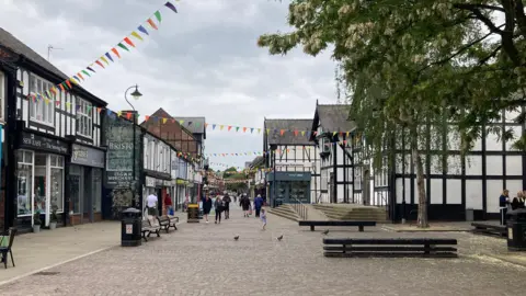 A view of shops in Northwich town centre. Many of the buildings are Tudor-style, with white walls and black beams.
