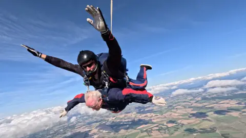 Blind Veterans UK Danny Gibbon during a tandem parachute jump strapped beneath a professional with land and clouds below them