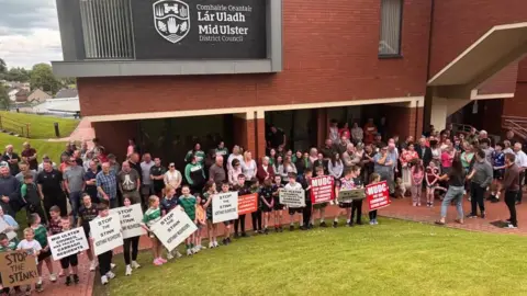 A large group of mainly children holding placards saying stop the stink. They are standing in front of an inflatable globe.