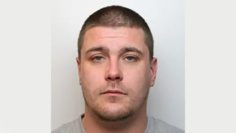 Wiltshire Police A mugshot of Grant Walker. He has short brown hair and grey-green eyes. He is wearing a grey t-shirt and standing against a grey background. He is looking at the camera with a blank expression.