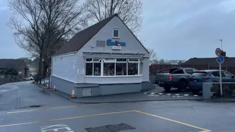 The exterior of Beeton's Fish and Chip shop. It is a two-storey building with a large sloped roof, and a sign on the front which says Beeton's Fish and Chips in blue writing.