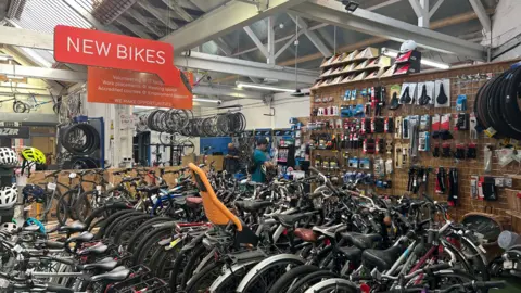 A variety of bikes lined up inside a shop with a sign that reads "new bikes" hanging from the roof.