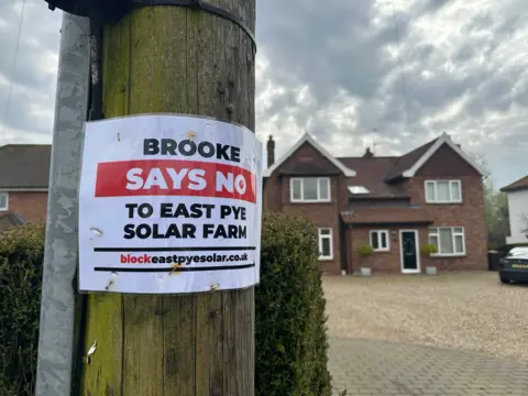 Jenny Kirk/BBC A close-up on a telegraph pole which has a sign stuck to it saying "Brooke Says No To East Pye Solar Farm"