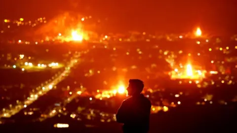 A man stands on the Cave Hill in Belfast staring out at a range of bonfires.