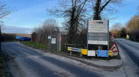 LDRS A road leading to the gateway of a landfill site in Lower Compton with a large sign with the Hills Waste Solutions logo written on it. 