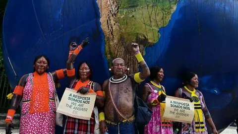 AFP via Getty Images Indigenous people pose next to a giant inflatable globe during the "Indigenous People Global March" at the COP30 UN Climate Change Conference in Belem, Para state, Brazil, on November 17, 2025.