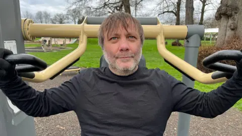 A man sat on a piece of outdoor gym equipment for working out his arms