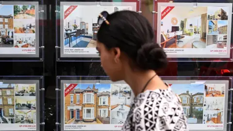 Shutterstock A woman looks at a house for sale sign in an estate agent's window