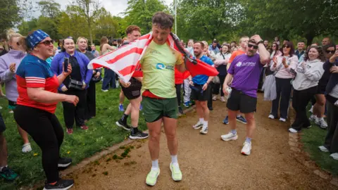 Liam McBurney/PA Wire Jordan Adams is in a light green T-shirt in the middle of the photo, with dozens of people looking towards him. Trees are in the background from left to right on the image.