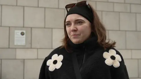A woman wearing a black coat with white flowers, a black bandana, and sunglasses on top of her head