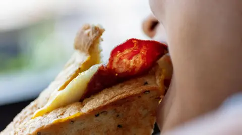 Getty Images Person eating a cured meat and cheese sandwich 