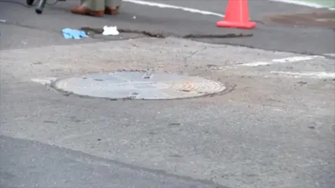 A covered manhole on a street with an orange cone nearby 
