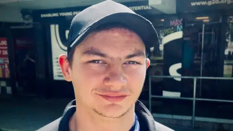 Close-up portrait of Connor McGurn wearing a black baseball cap and dark jacket, standing outdoors in front of a building entrance with signage and railings visible in the background.
