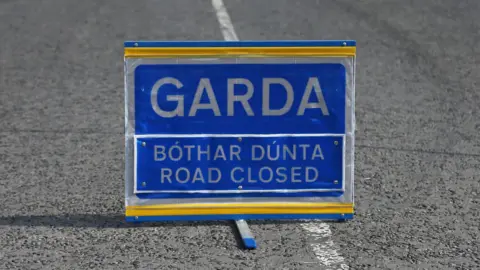 A blue Garda road closed sign sits in the middle of a road.