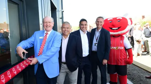 Chris Vaughan/Lincoln City Lincoln City staff with the ribbon at the new community hub, alongside a mascot