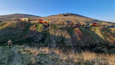 West Yorkshire Fire and Rescue Fire engines scattered across the brown moors with firefighters in action.