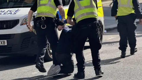 BBC A man being taken away by officers