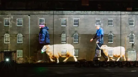 Maltings Trust A projection on the walls of the barracks shows two women in blue clothing walking sheep