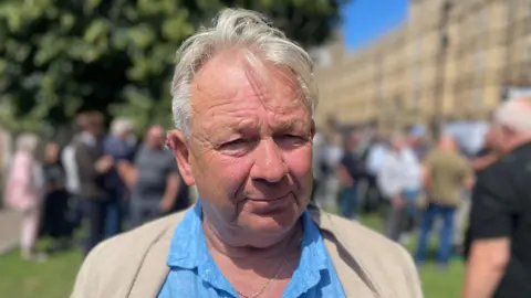 Campaigner Charles Chiverton wearing a blue shirt and beige jacket standing outside the Houses of Parliament.