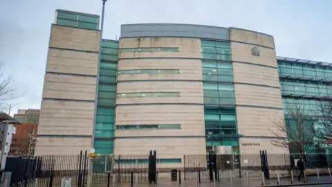 PA Media A large courthouse with white brick and green tinted windows. A black gate surrounds the building.