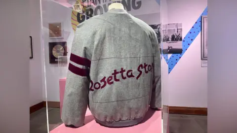 A 1982 Rosetta Stone Canadian tour jacket. It is a grey jacket with burgundy writing that says 'Rosetta Stone'.