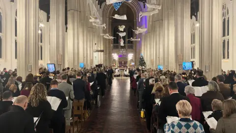 Jon Wright/BBC A photo from the back of a Cathedral, with rows of chairs full of people and a choir at the front.