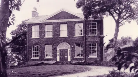 Bolton Council A black and white photograph of Rock Hall in Farnworth. The image shows the manor house with its Georgian windows and the building is surrounded by trees.