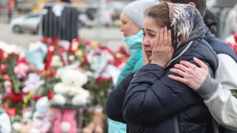 A woman puts her hands to her face asshe looks at the makeshift memorial in Krasnogorsk, outside Moscow.