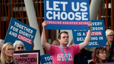 Getty Images Protesters hold colourful signs in favour of assisted dying 