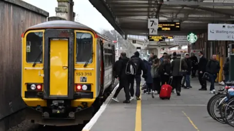 Midlands Connect A train at Shrewsbury station with passengers disembarking from the right hand side of the train onto the platform with a sign above saying 7b. Some bikes stored in a rack can be seen on the right of the image.
