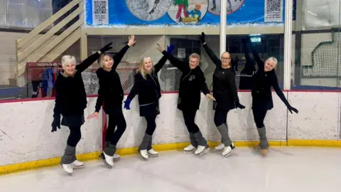 Girls on Tour The ladies are wearing their black uniform with their arms outstretched on the ice.