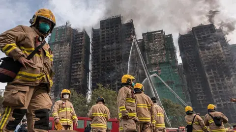 Getty Images Firemen get ready after a major fire swept through several apartment blocks at the Wang Fuk Court