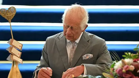 Reuters King Charles signs a book of condolence during his visit to Southport Town Hall