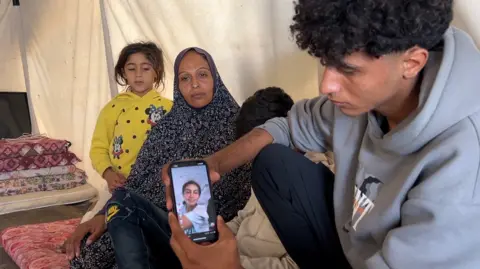 Family members in the tent show photos of Aya on mobile phones 