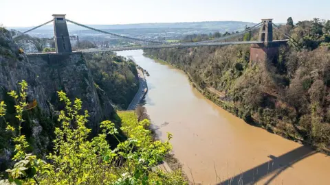 The Clifton Suspension Bridge seen from above over the River Avon. Bristol can be seen in the distance.