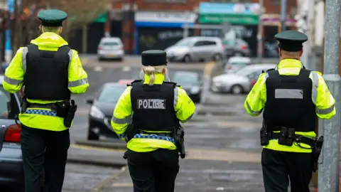 Police officers walking away from the camera, in full hi-vis police gear. 