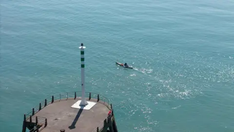 ファーガス・ケンタニーは、海のボートを見せている景色であり、太陽は水を反映しています。金属上の白と緑の前進。