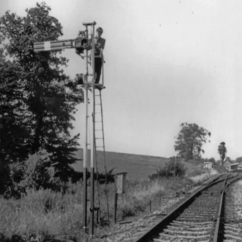 Paul Antell Collection Black and white photo of a young Paul Antell up the ladder of an abandoned railway signal alongside the abandoned track