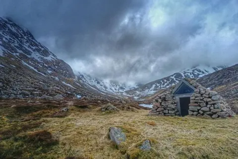 Iain Kelman A rock refuge in the foreground, with snow-capped hills behind.
