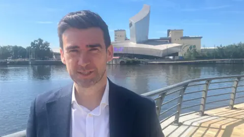 Photograph of Peter Rowe from the renewable energy firm Cubico. The picture is taken with Salford Quays and the Imperial War Museum North in the background.