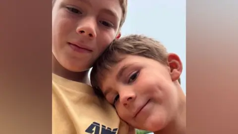 Two young boys with short, light-brown hair lean in for a photo