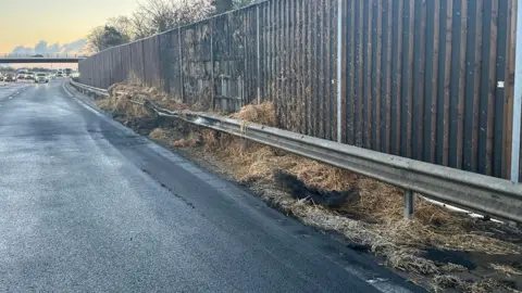 National Highways Motorway lane with hay strewn along the edge and a crumpled barrier.