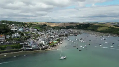 Aerial view of Salcombe town with turquoise blue estuary and boats moored with a pontoon and jetties into the estuary from the town.