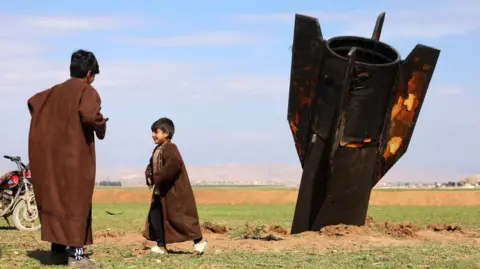 EPA People stand next to an Iranian missile that fell in the village of Qazaljo in Syria.