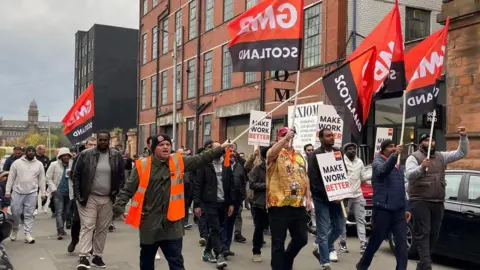 Uber drivers protest  in Glasgow. Men carry placards saying Make Work Better and red and white GMB flags 