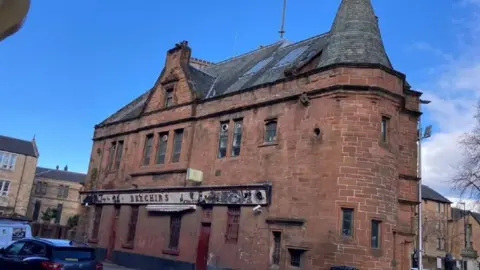 An old redbrick building with a black roof and worn sign 